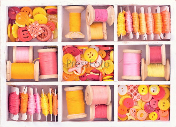 Collection of yellow, red, pink spools  threads on in a white wooden box