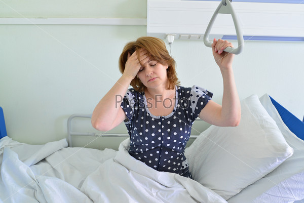Female patient with headache on a bed in hospital ward