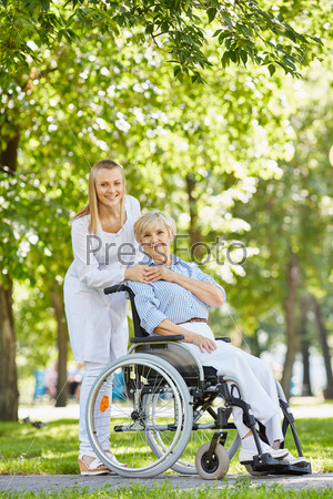 Young nurse and senior patient in a wheelchair looking at camera in park