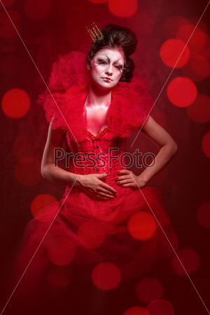 Red Queen. Woman with creative make-up in fluffy red dress posing over glowing lights background