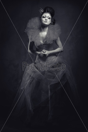 Queen. Woman with creative make-up in fluffy dress posing indoors. Black and white