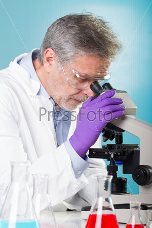 Focused senior life science professional routine screening the microscope slides in the cell laboratory. Lens focus on the researcher\'s face.