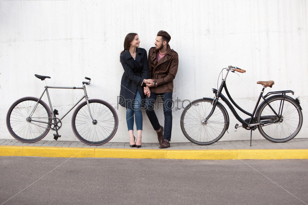Young couple standing against the wall and hugging in city. two bikes stand next