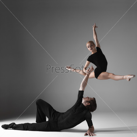 The two young modern ballet dancers in black suits over gray studio background