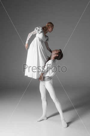 Two young classic ballet dancers practicing. attractive dancing performers  in white suits over gray background