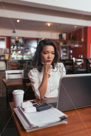 Serous Vietnamese bar owner working on laptop in her bar