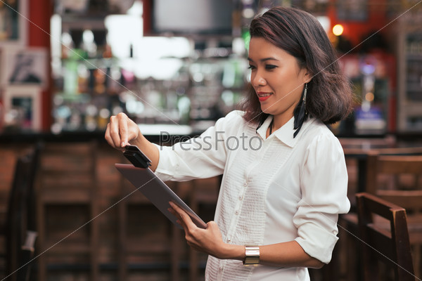 Bar owner using credit card reader on the tablet to swipe payment