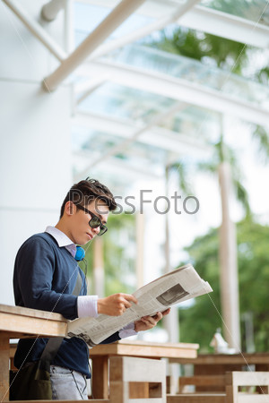 Young man in outdoor cafe reading newspaper