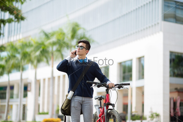 Asian young man with a bicycle talking on the phone