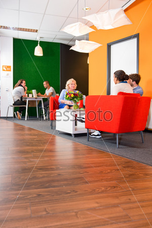 Modern styled, colorful business lounge, with several project teams sitting at tables during informal meetings