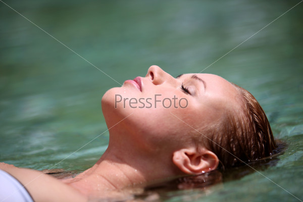 Woman floating in swimming pool, stock photo