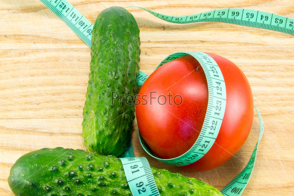 Cucumber and tomato with measuring tape over desk  - the concept of dieting and health