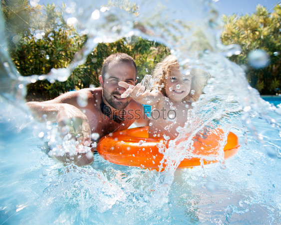 Happy family playing in blue water of swimming pool on a tropical resort at the sea. Focus on children`s hand and splash, shot was taken with waterproof box