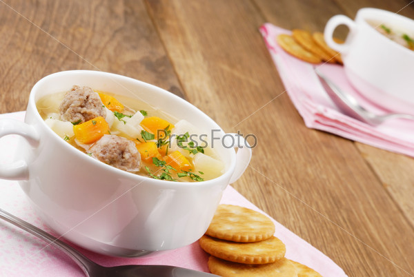Homemade soup with meatballs and crackers on the wooden table