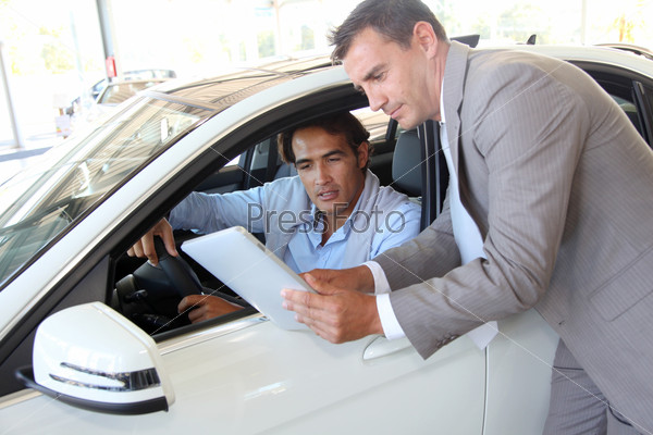 Car seller with car buyer looking at electronic tablet