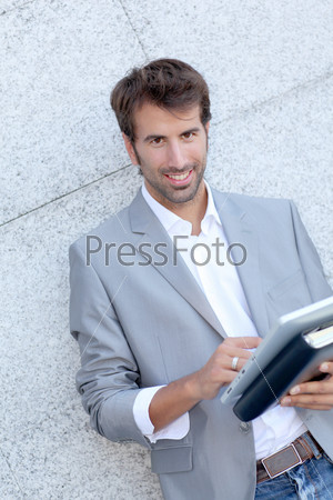 Handsome man leaning on wall with electronic tablet