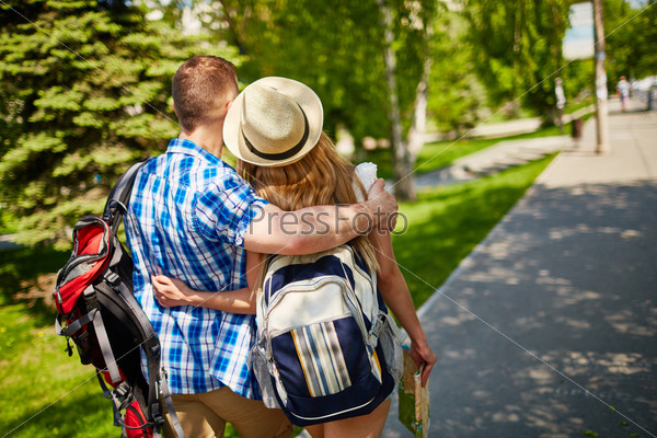 Amorous couple with backpacks walking in urban environment