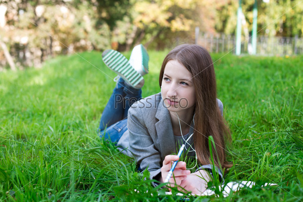 Student with headphones lying on grass and looking away