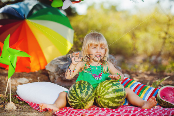 Cute little girl playing with watermelons in summer park outdoors