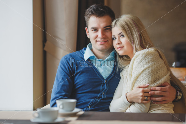 Portrait of happy young couple embracing each other and drinking coffee in a cafe