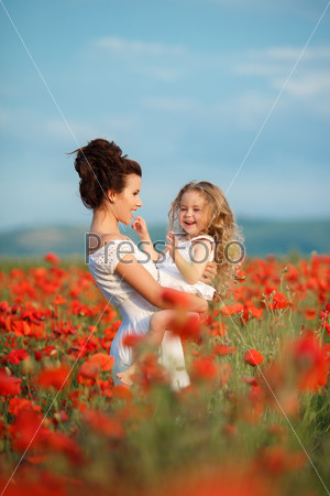 Happy family resting on the poppy field. Mother playing with her toddler child in poppy field. Happy joyful woman having fun with her baby girl in a field of poppies
