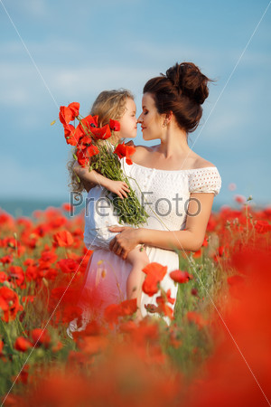 Happy family resting on the poppy field. Mother playing with her toddler child in poppy field. Happy joyful woman having fun with her baby girl in a field of poppies