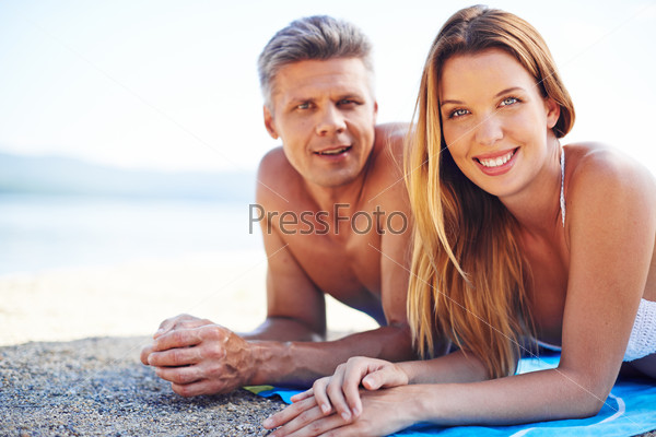 Amorous couple looking at camera while relaxing on the seaside , stock photo