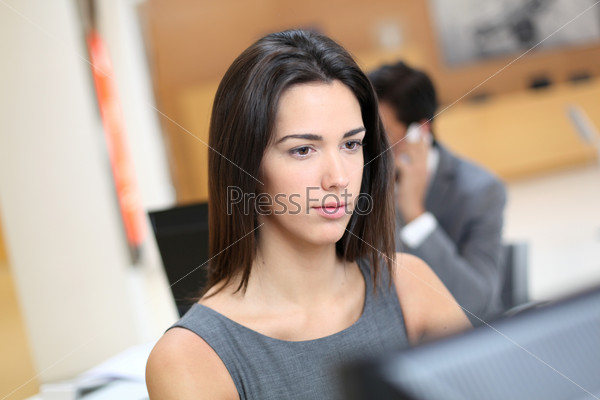 Woman working in office in front of desktop computer, stock photo