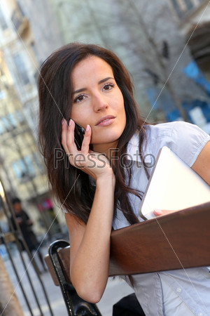 Young woman sitting on public bench with mobile phone