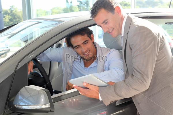 Car seller with car buyer looking at electronic tablet