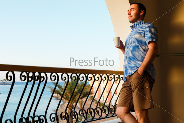 handsome guy standing on balcony in luxury hotels in Egypt at sunset and drinking tea.