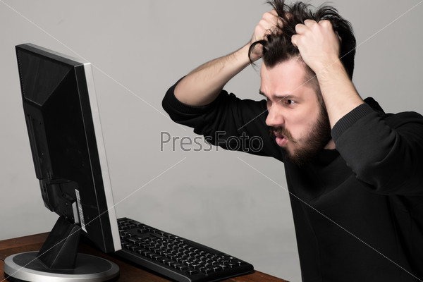 Funny and crazy man using a computer on gray background. man\'s hands on his head