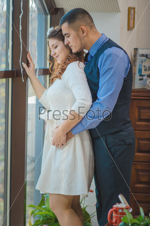 The young loving couple embraces and are by the big window. Wedding