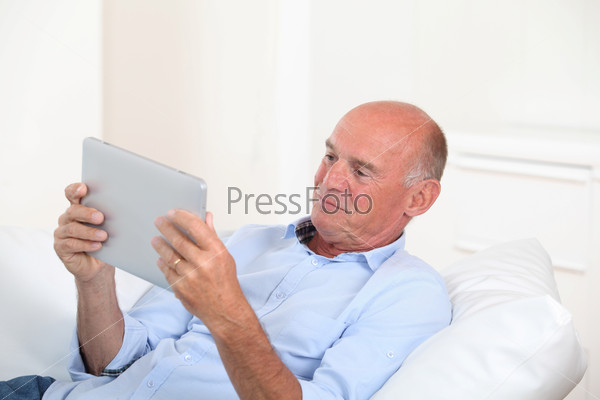 Senior man using electronic tablet at home, stock photo