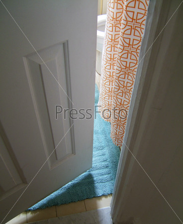 View through narrowly open door onto a blue rug and orange curtain