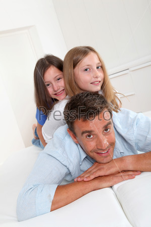 Man lying down on sofa with girls on his back