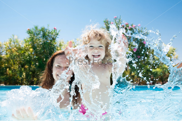 Happy family playing in blue water of swimming pool on a tropical resort at the sea. Summer vacations concept
