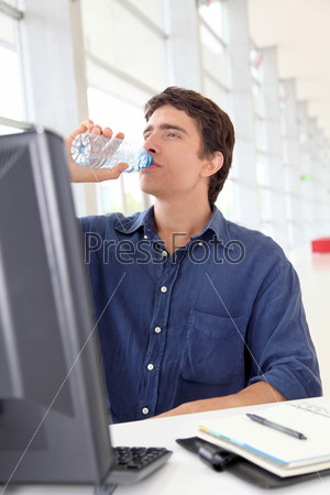 Office worker drinking water in front of desktop computer