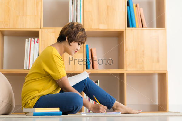 Woman sitting on the floor and writing ideas in the notepad