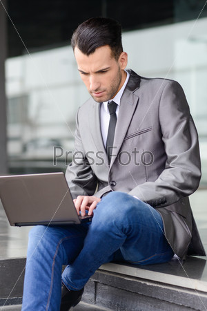 Portrait of attractive young businessman typing in a laptop computer in office building