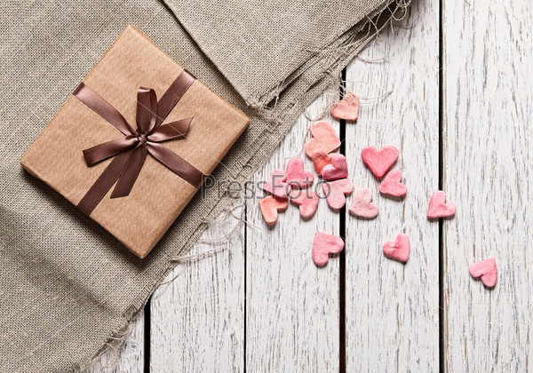 Gift box with heap of small hearts on white wood table.