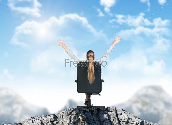 Businesswoman sitting in chair on mountain top, rear view