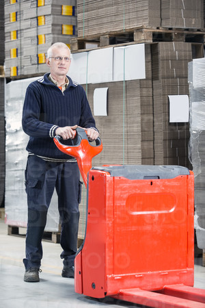 Full length portrait of confident male worker standing with handtruck at warehouse
