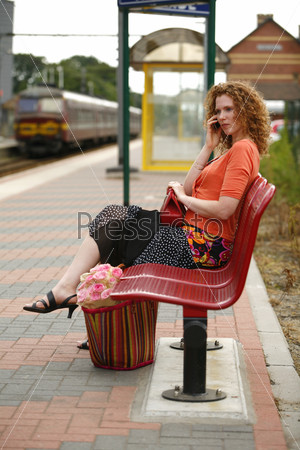 Young woman on phone while sitting on the bench and waiting for train on the platform