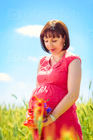 pregnant woman standing in a field in the summer dreaming of the future child