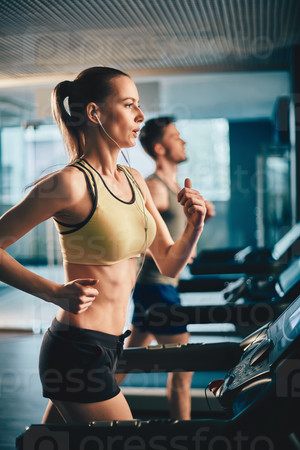 Fit girl with earphones running on treadmill in sports club