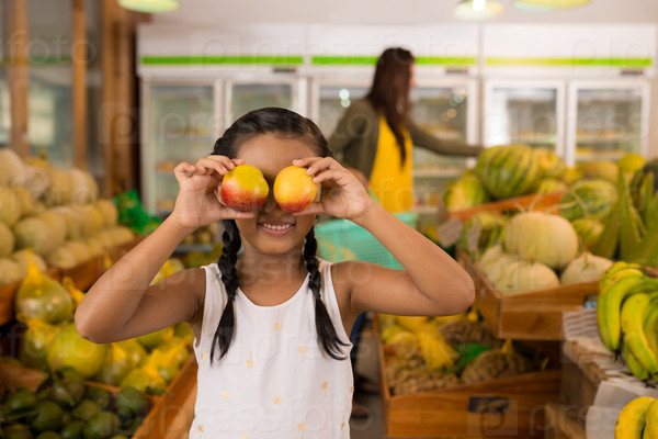 Girl in the grocery store holding peaches in front of her eyes: organic shopping concept