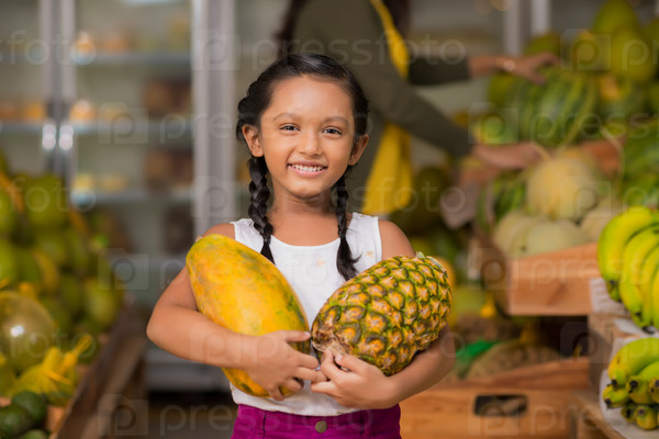 Portrait of happy Indian girl with pineapple and melon in her hands
