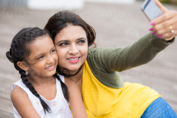 Smiling Indian mother and daughter hugging and taking selfie