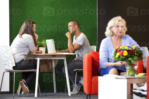 Businesspeople discussing while sitting at table in modern office lobby